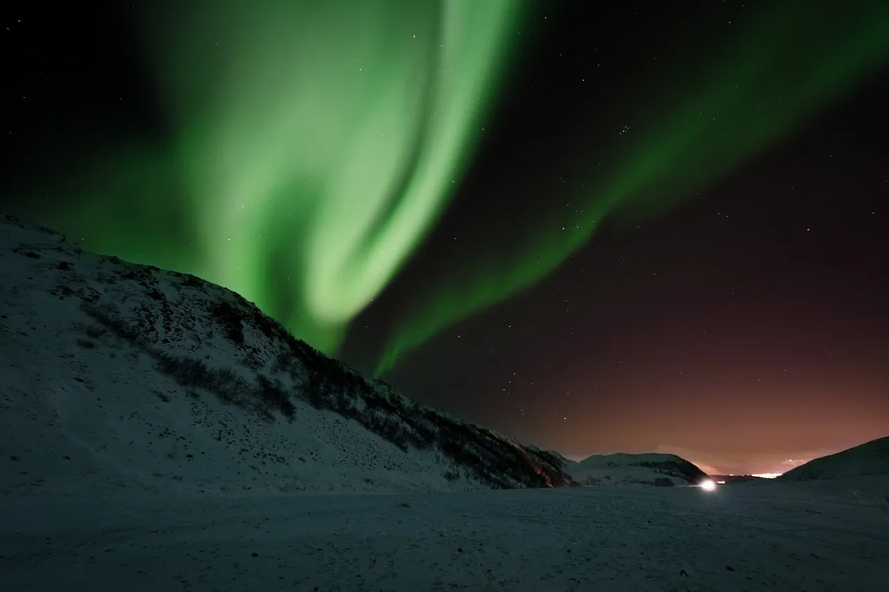 Green northern lights over snow-covered mountains in northern Norway